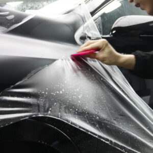Woman applying PPF in a matte finish to a gray car