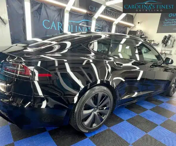 A side profile view of the black Tesla in a professional workshop.