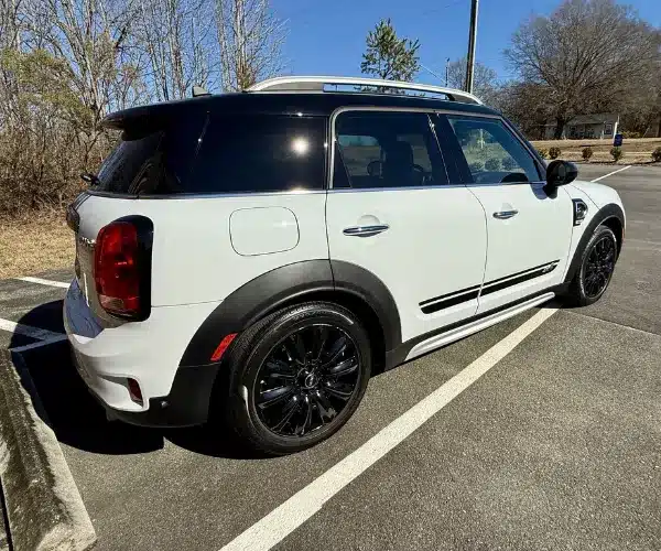 A rear three-quarter view of a white compact SUV featuring a black roof, roof rails, and black multi-spoke wheels in a paved parking lot.