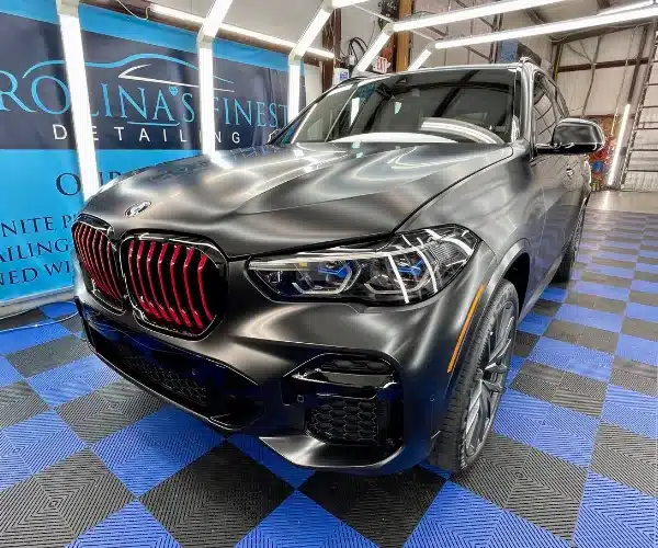 view of a luxury car parked inside a brightly lit detailing garage, showcasing a flawless, high-gloss finish after a paint protection film installation