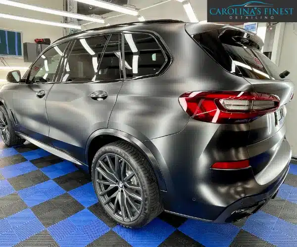 view of a luxury car parked inside a brightly lit detailing garage, showcasing a flawless, high-gloss finish after a paint protection film installation