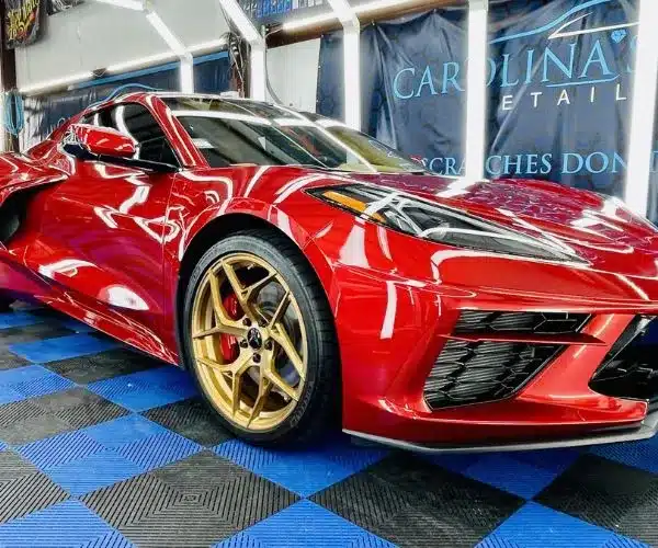 view of a high-gloss red Corvette sports car with gold wheels inside an auto detailing garage