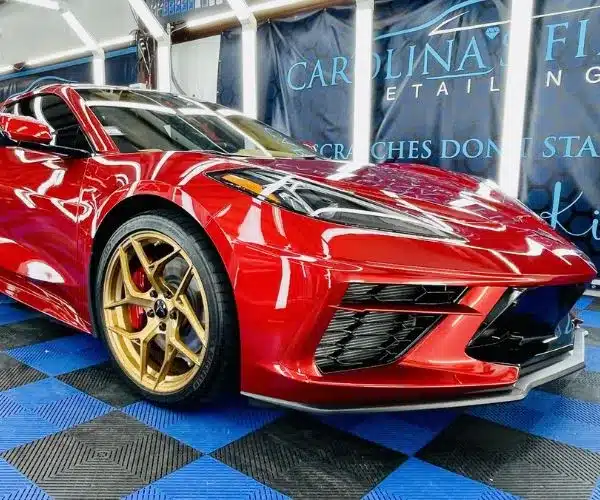 view of a high-gloss red Corvette sports car with gold wheels inside an auto detailing garage