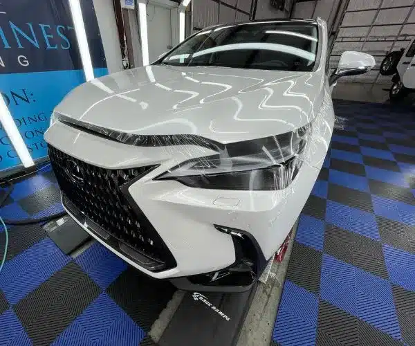 view of a white Lexus SUV on race ramps receiving clear paint protection film over the hood and headlights