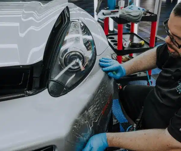 view of a white Lexus SUV on race ramps receiving clear paint protection film over the hood and headlights