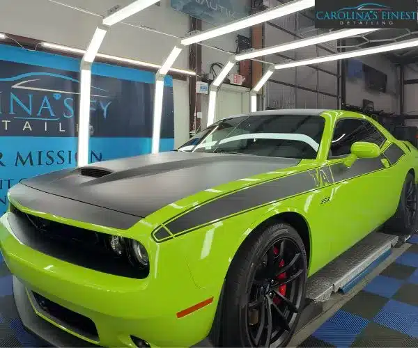 Lime green Dodge Challenger T/A with a matte black hood, roof, and side stripes parked inside an auto detailing garage under LED lighting.