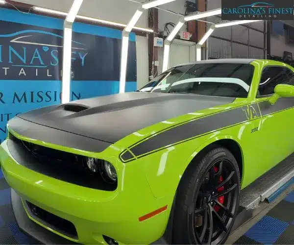 Lime green Dodge Challenger T/A with a matte black hood, roof, and side stripes parked inside an auto detailing garage under LED lighting